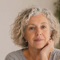 Woman with curly gray hair wearing a gray sweater indoors.