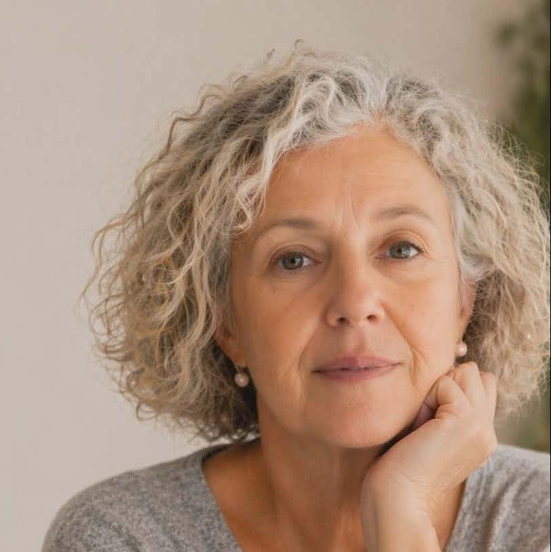 Woman with curly gray hair wearing a gray sweater indoors.